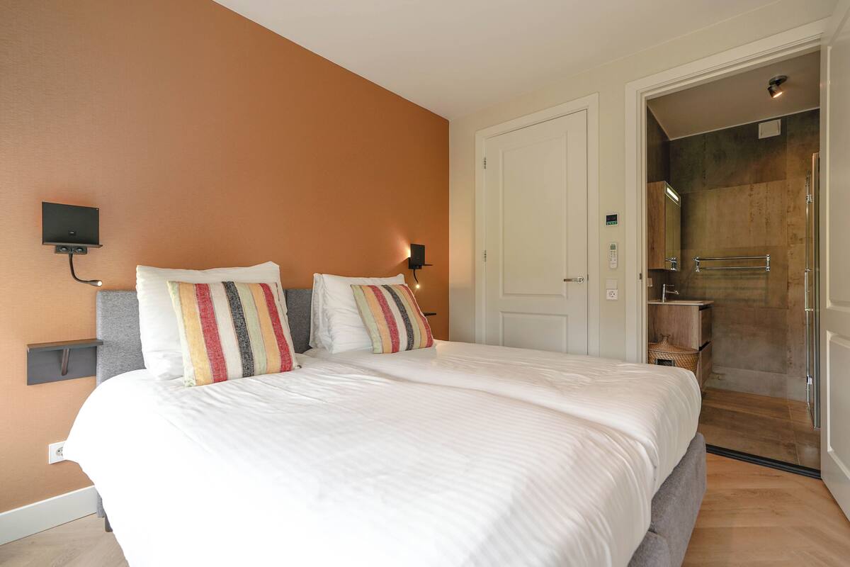 A hotel room with a large bed, a nightstand, a wall-mounted TV, and a door leading to a bathroom.