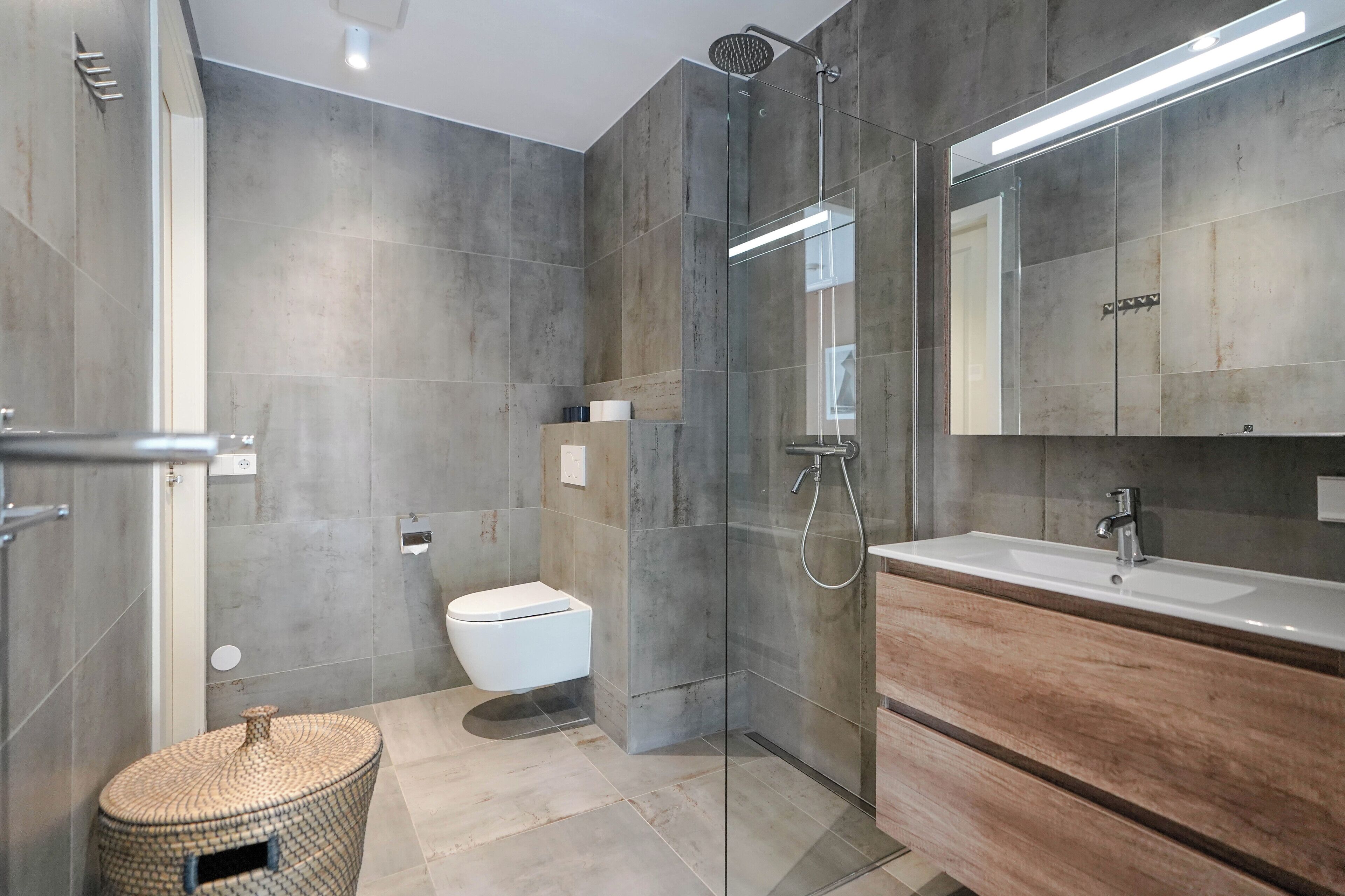 Un baño moderno con ducha de vidrio, inodoro blanco y tocador de madera con espejo.