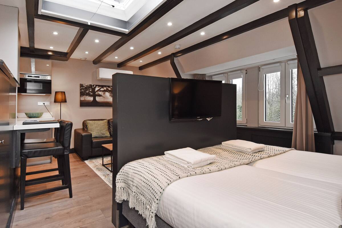 A modern bedroom with a large bed, a desk with a chair, a TV mounted on the wall, and a window with curtains.