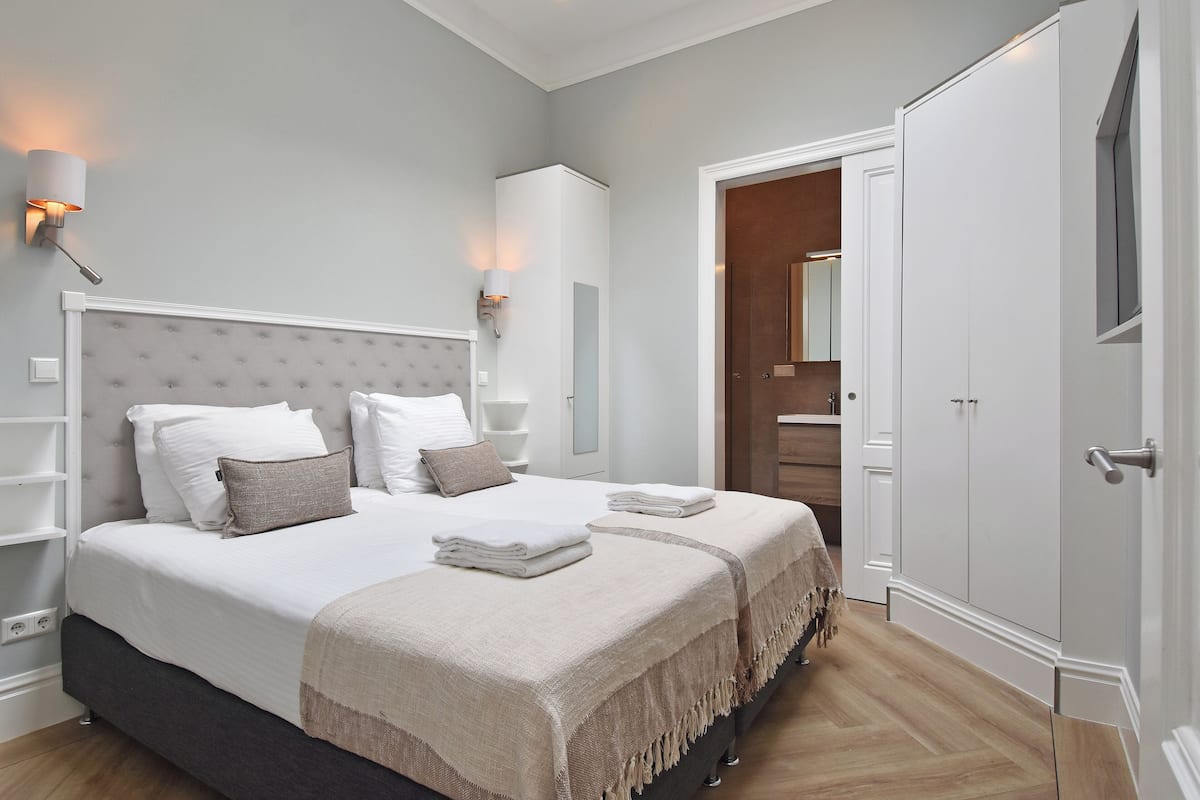 A modern bedroom with a large bed, bedside tables, a wardrobe, and a mirror.