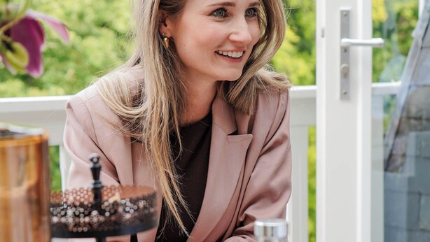 Une personne est assise à une table devant un présentoir à trois niveaux rempli de desserts, une bouteille d’eau et un verre.