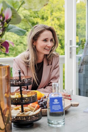 Une personne est assise à une table devant un présentoir à trois niveaux rempli de desserts, une bouteille d’eau et un verre.