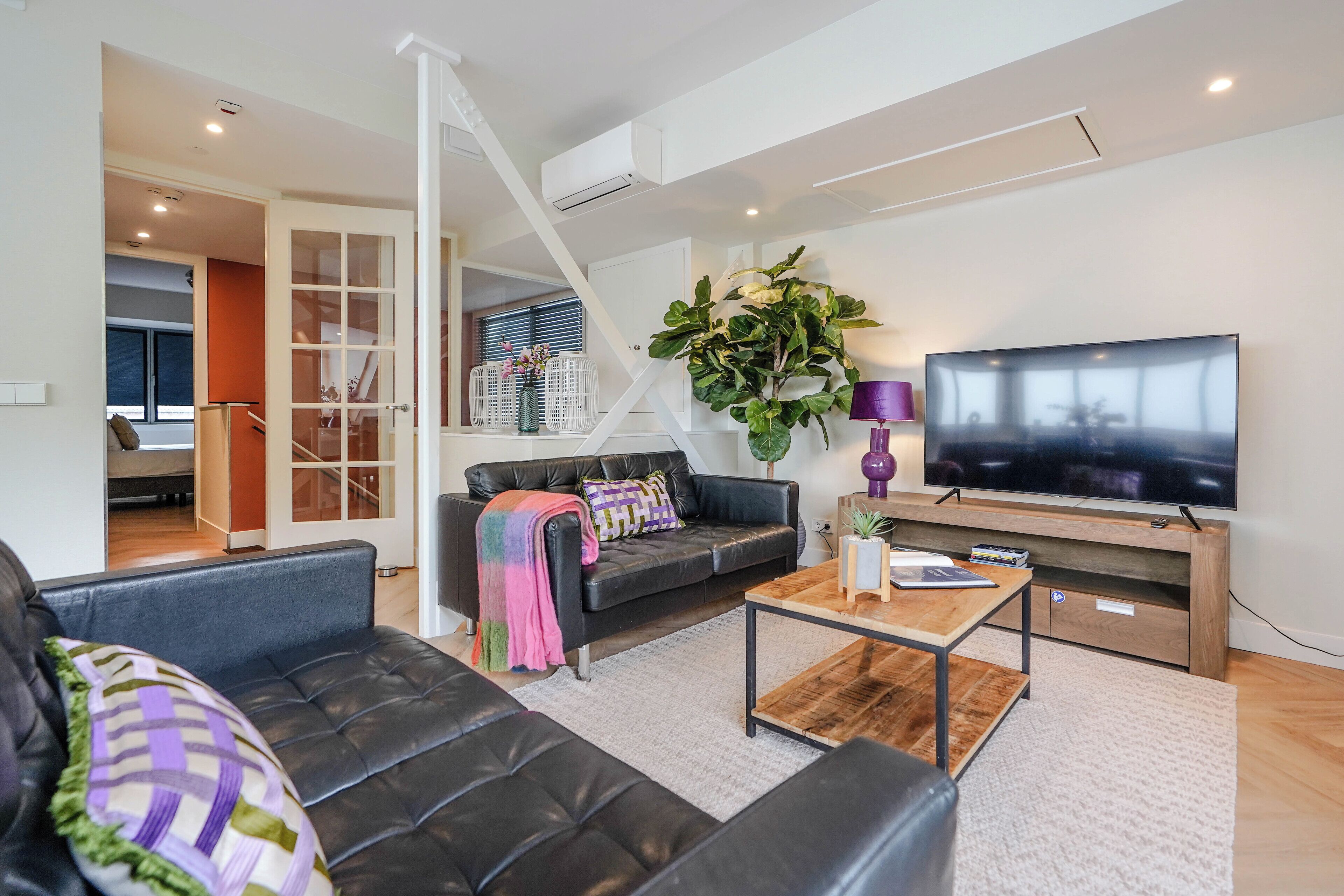 A modern living room with a black leather sofa, a wooden coffee table, and a large flat-screen TV.
