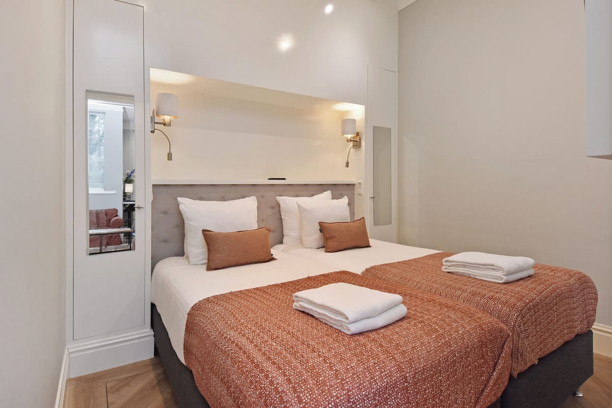 A modern hotel room with a large bed, two bedside tables, a mirror, and a wall-mounted light fixture.