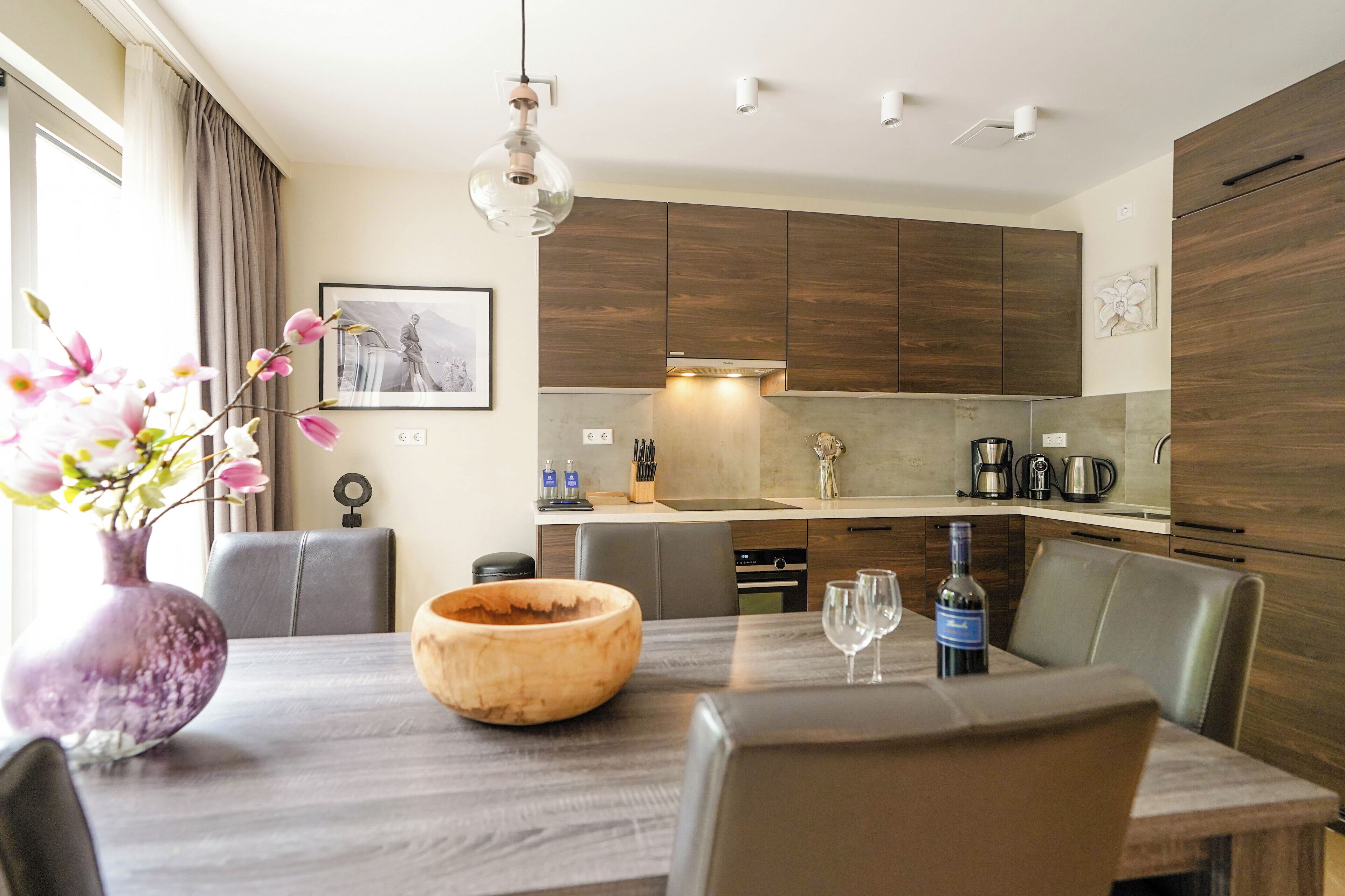 A modern kitchen with wooden cabinets, a dining table with chairs, and a vase with flowers.