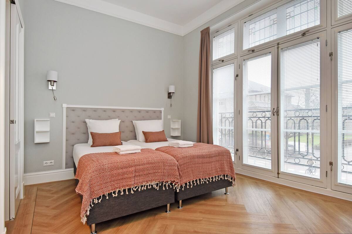 A bedroom with a large window, a bed with a headboard, and two bedside tables.
