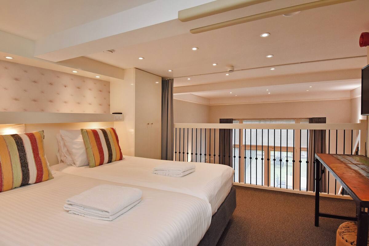 A hotel room with two beds, a desk, and a balcony with a view.