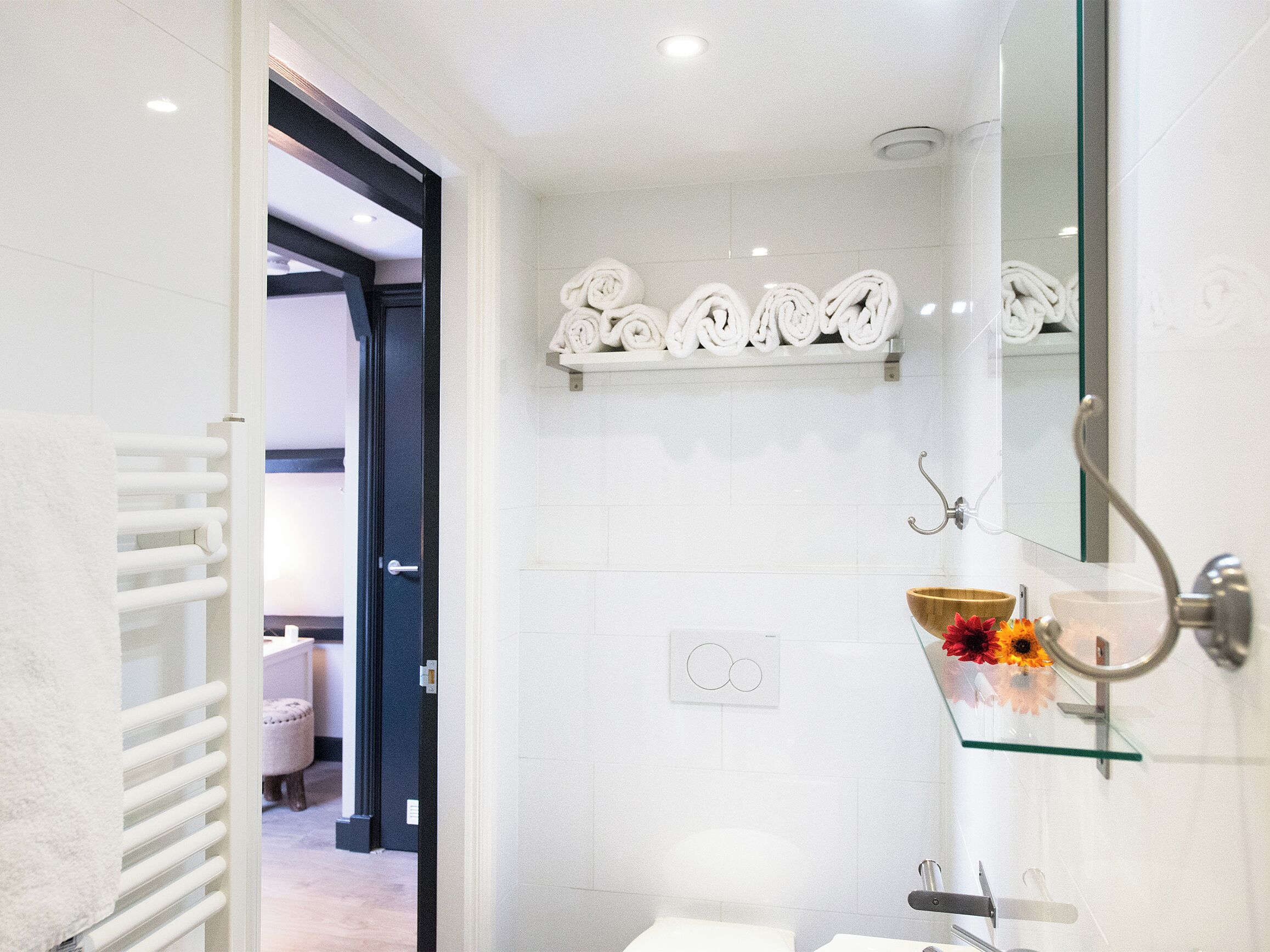 A modern bathroom with a glass shower enclosure, a white sink with a wooden bowl, and a towel rack with neatly folded towels.