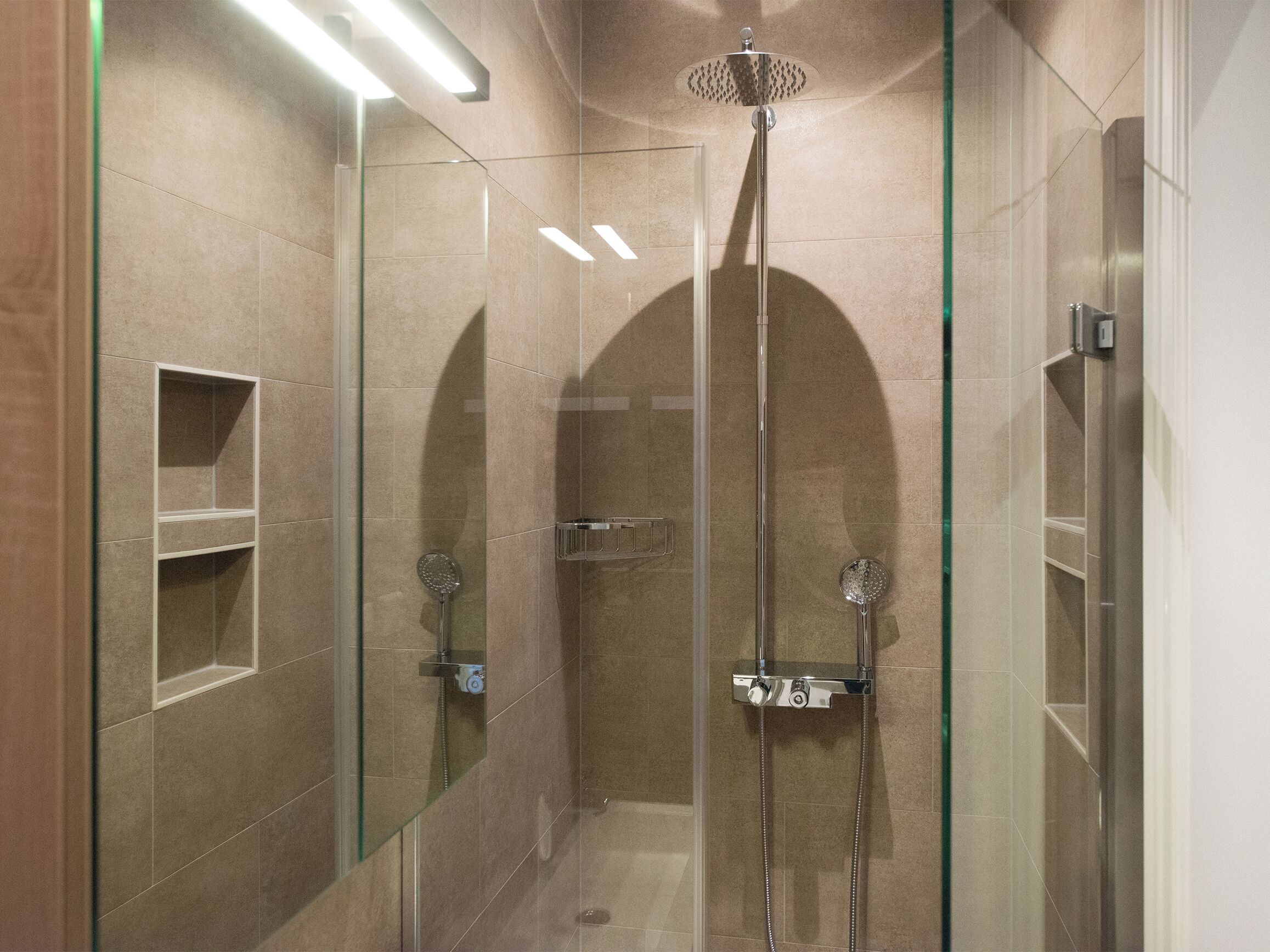 A modern shower with a glass enclosure, a handheld showerhead, and a wall-mounted faucet.