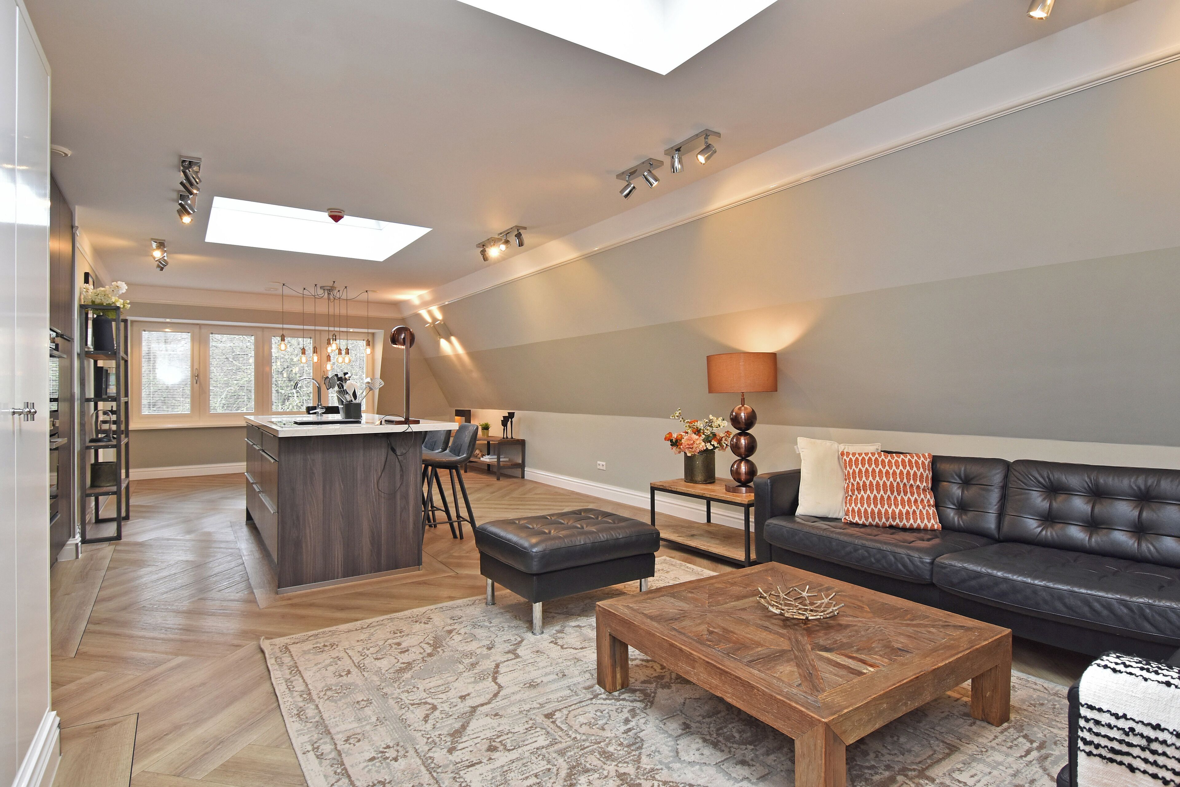 A spacious living area with a dark leather sofa, a wooden coffee table, and a central island with bar stools.