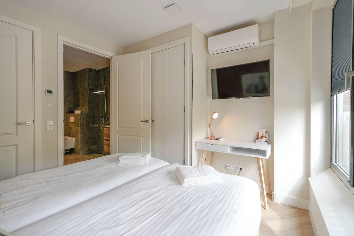 A hotel room with a large bed, a desk with a lamp, a TV, and a window.