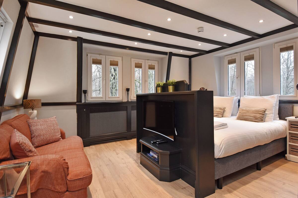 A cozy room with a bed, a sofa, a fireplace, and large windows.