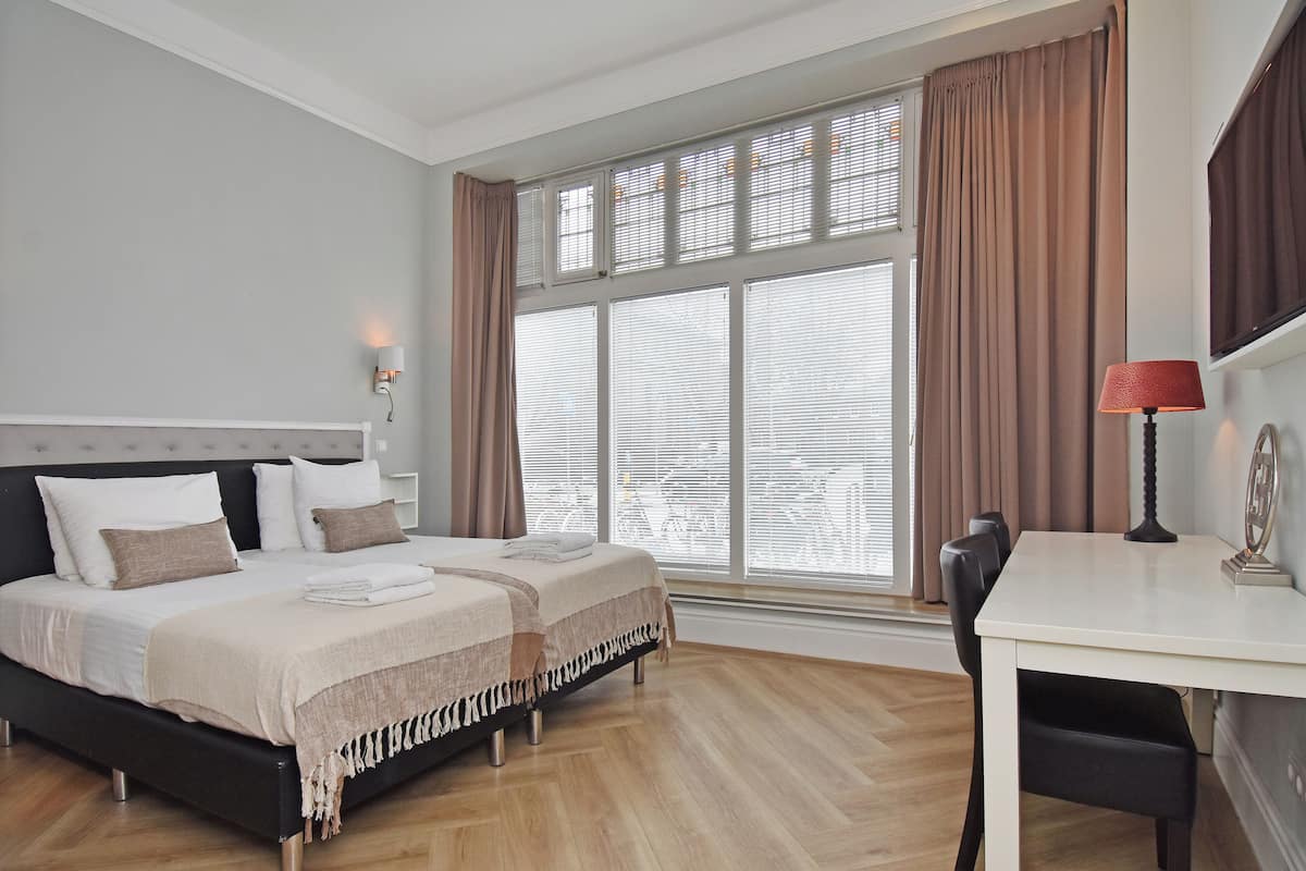 A bedroom with a bed, bedside table, lamp, and large window with curtains.