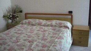 Une chambre à coucher avec un cadre de lit en bois, une couvre-lit à motifs floraux, une table de chevet avec des tiroirs et une plante en pot sur la table de nuit.