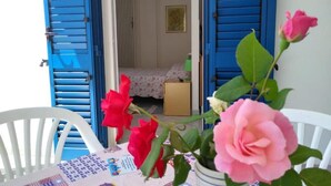Une pièce avec un lit, une petite table recouverte d’une courtepointe et un vase rempli de roses.