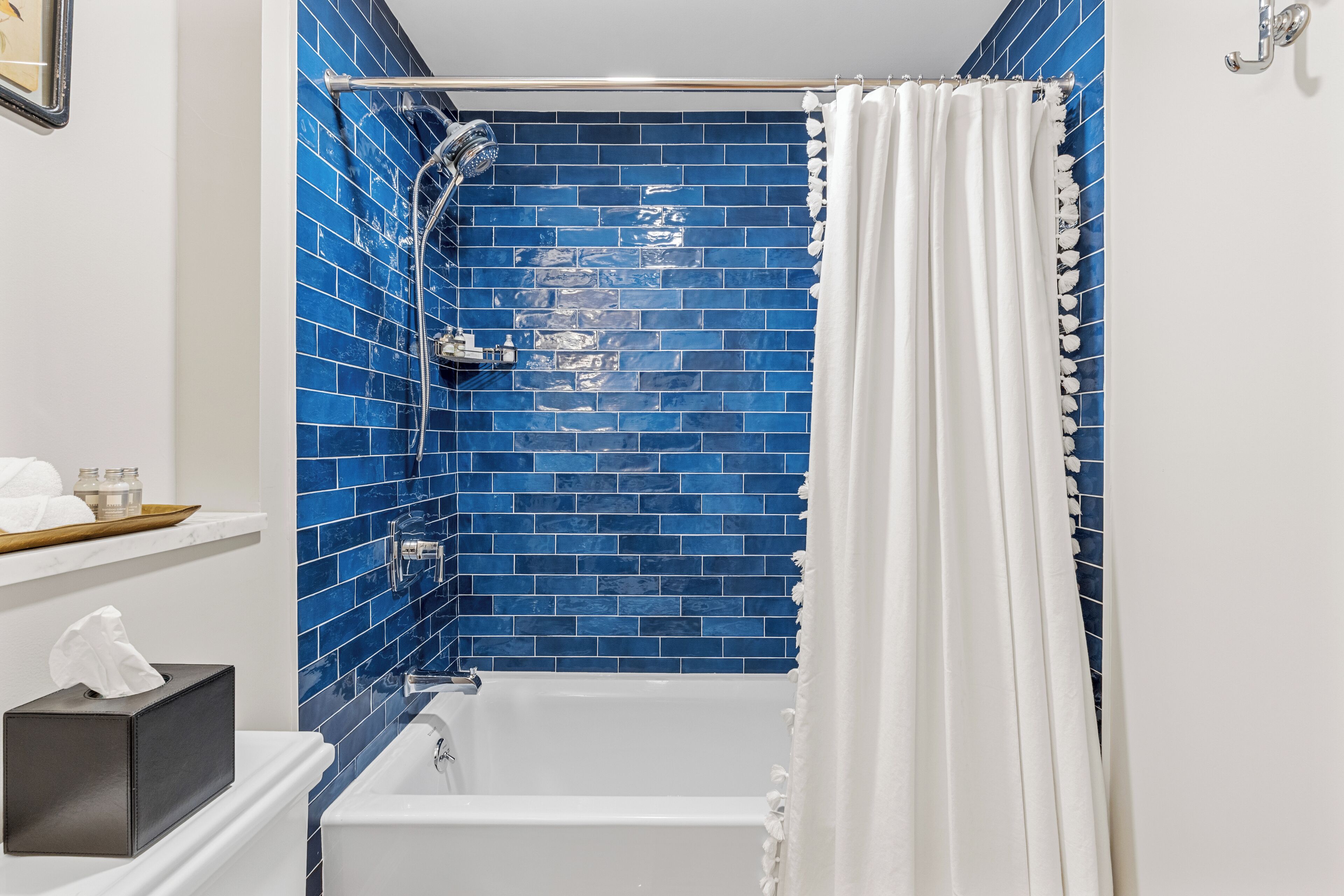 A bathroom with a white bathtub, blue-tiled walls, a showerhead, and a white curtain.