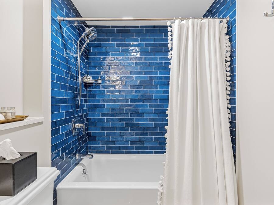 A bathroom with a white bathtub, blue-tiled walls, a showerhead, and a white curtain.