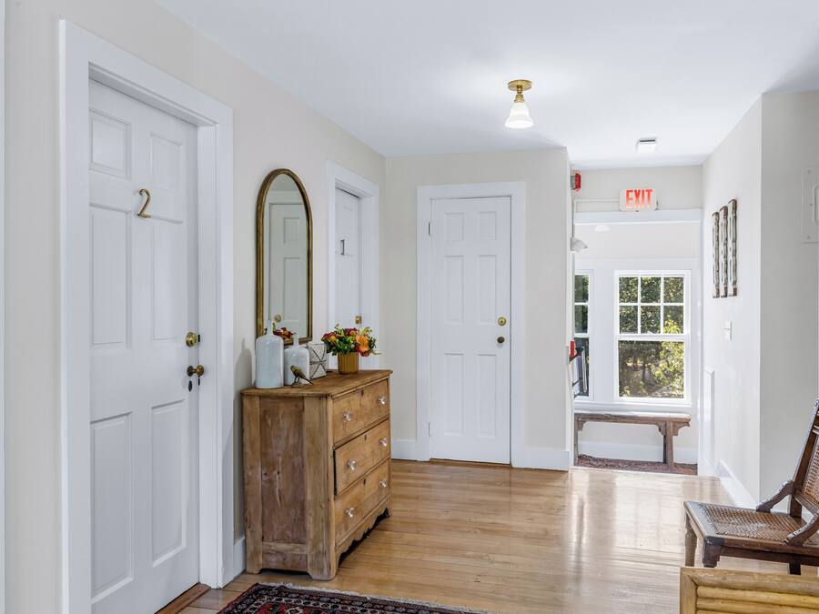 A hallway with white doors, a wooden dresser, a bench, and a window with a view.