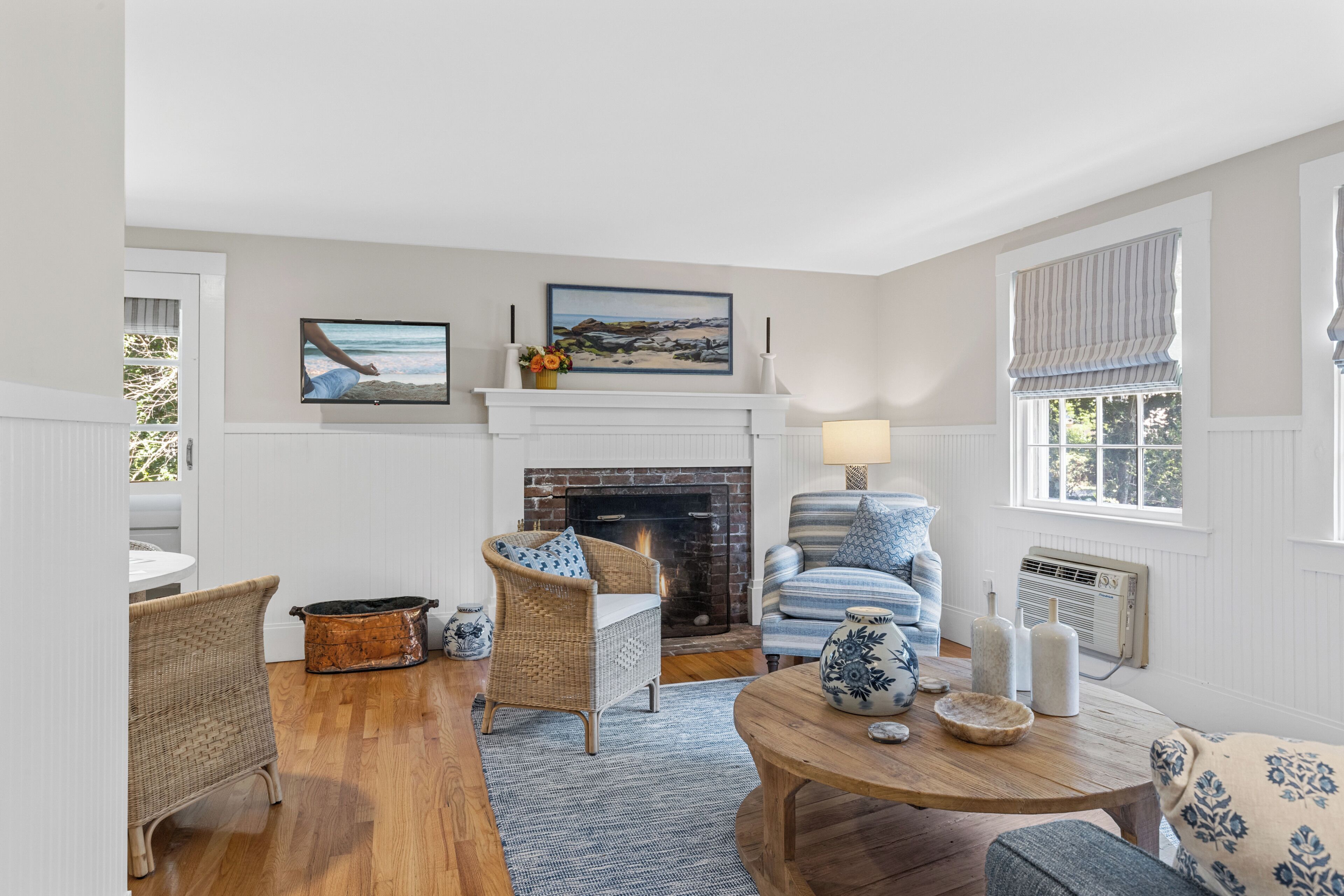 A cozy living room with a fireplace, wicker furniture, and a view of the outdoors.