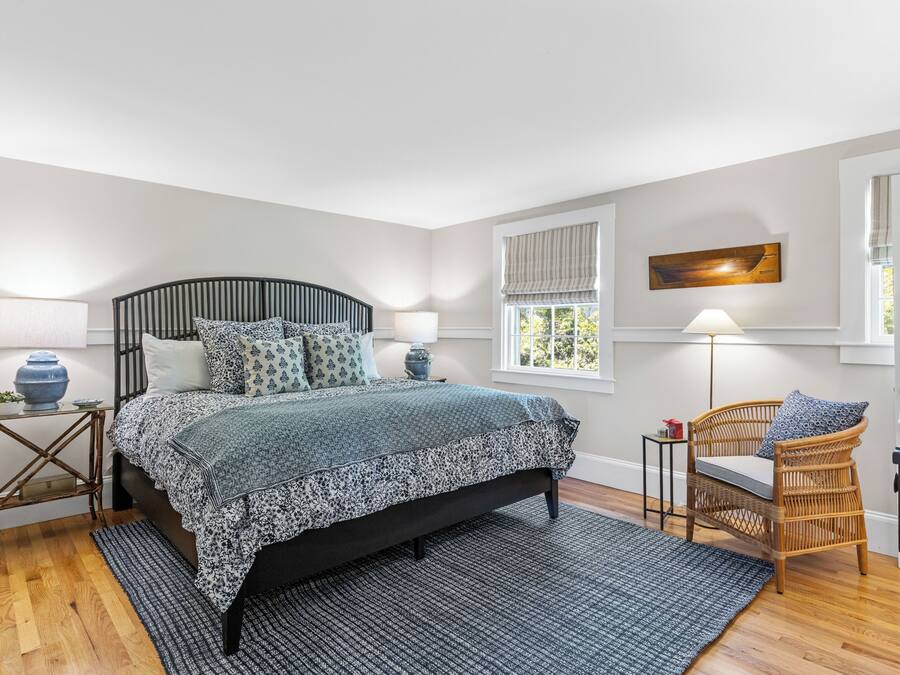 A bedroom with a bed, bedside tables, a chair, a window, and a painting on the wall.