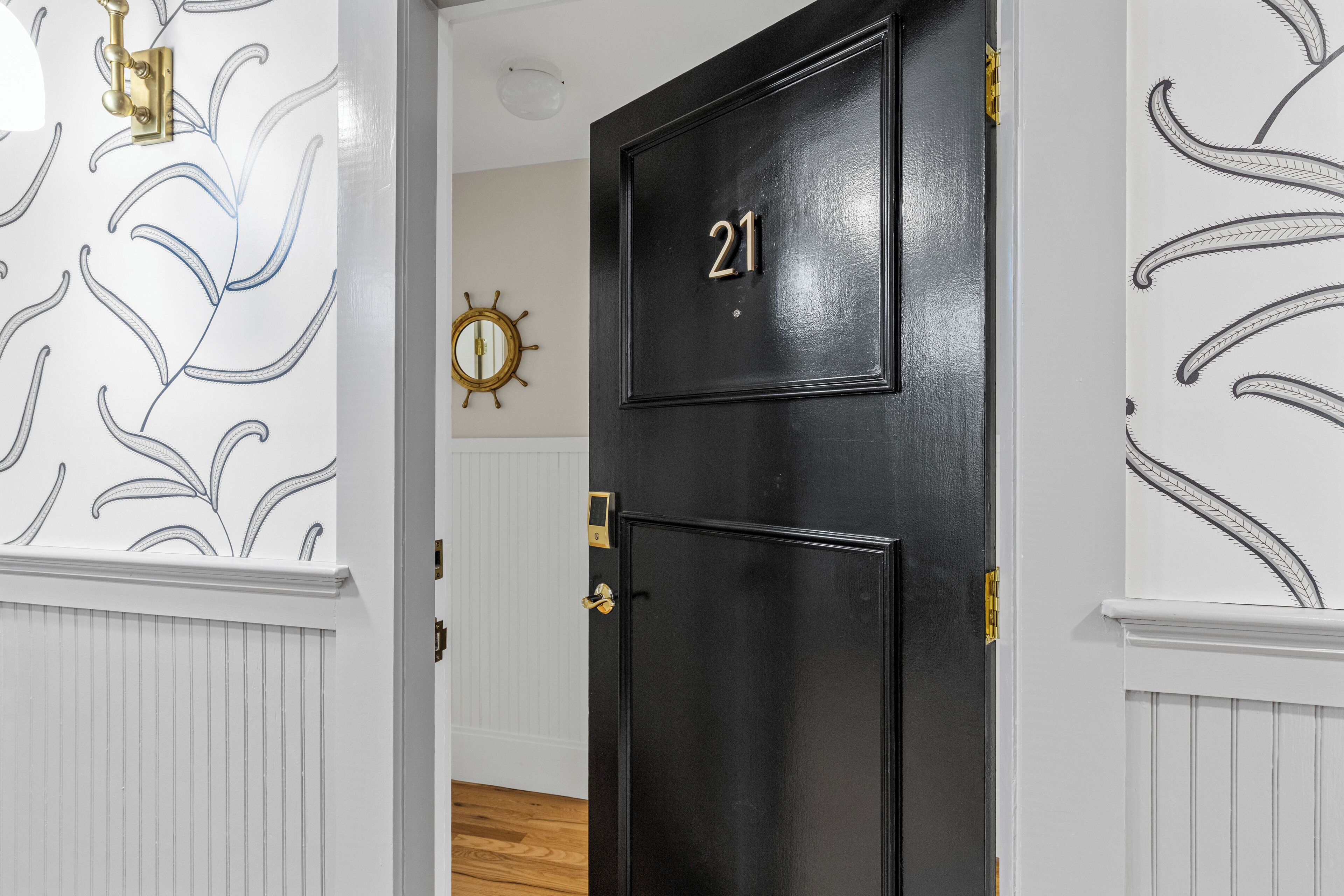 A black door with the number 21, white wainscoting, and a wall clock.