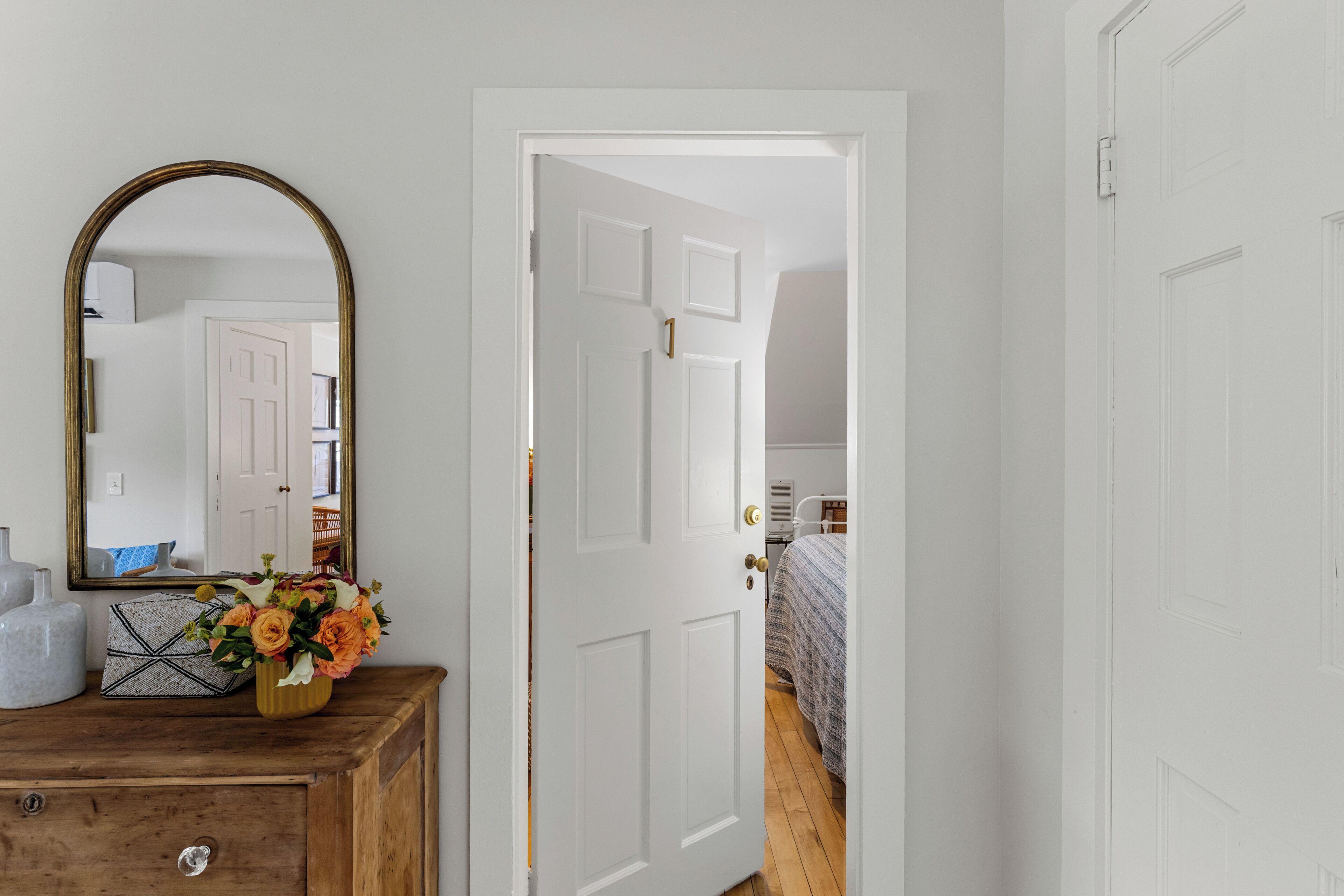 Una habitación con un aparador de madera, un espejo y una puerta blanca que da a otra estancia.