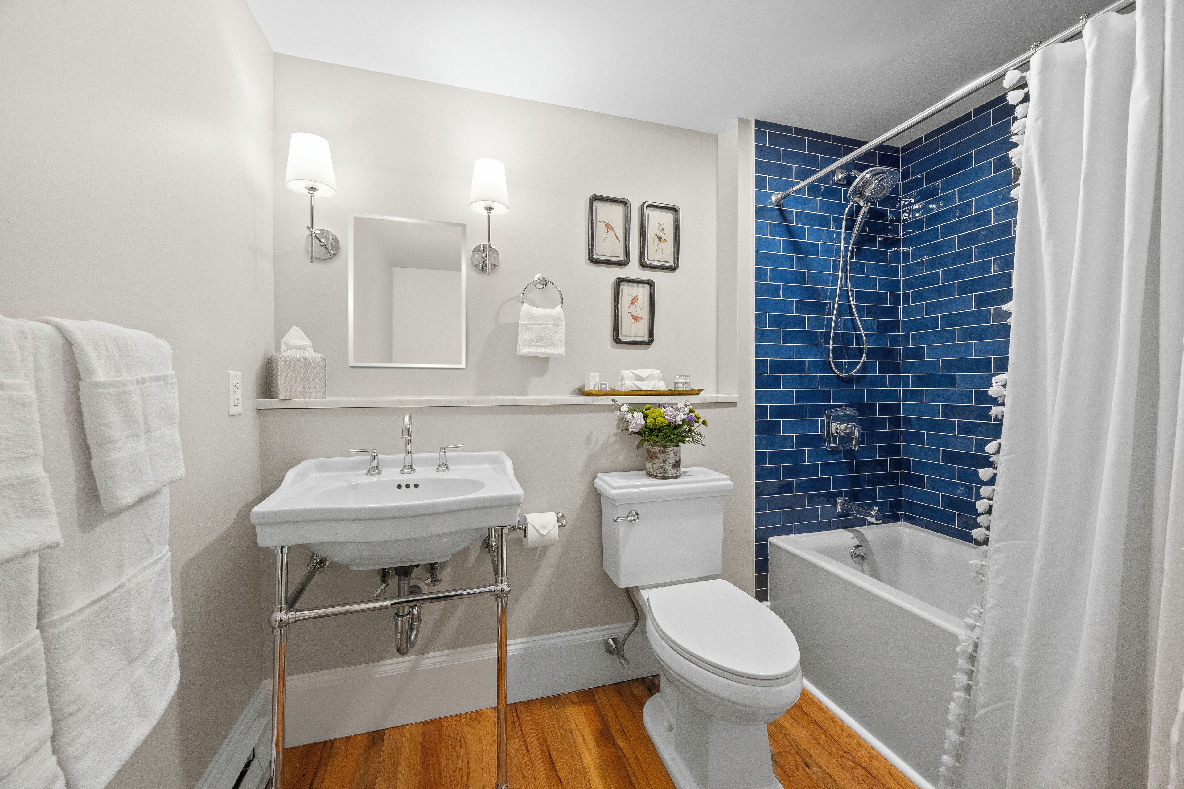 Une salle de bain avec un lavabo, des toilettes et une baignoire blancs, un mur de douche bleu et un plancher en bois.