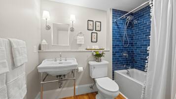 Une salle de bain avec un lavabo, des toilettes et une baignoire blancs, un mur de douche bleu et un plancher en bois.