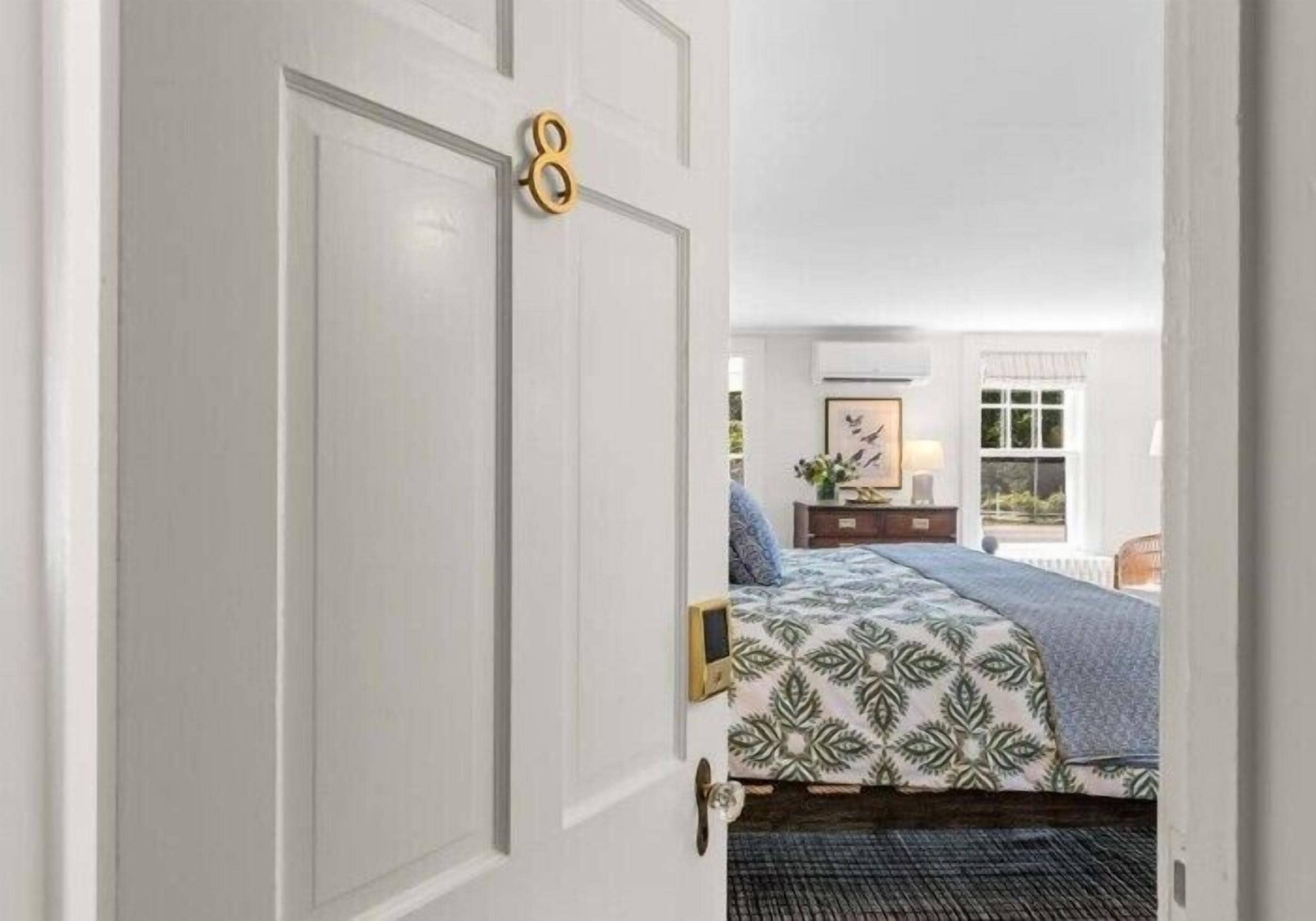A bedroom with a bed, a dresser, a window, and a door with a number.