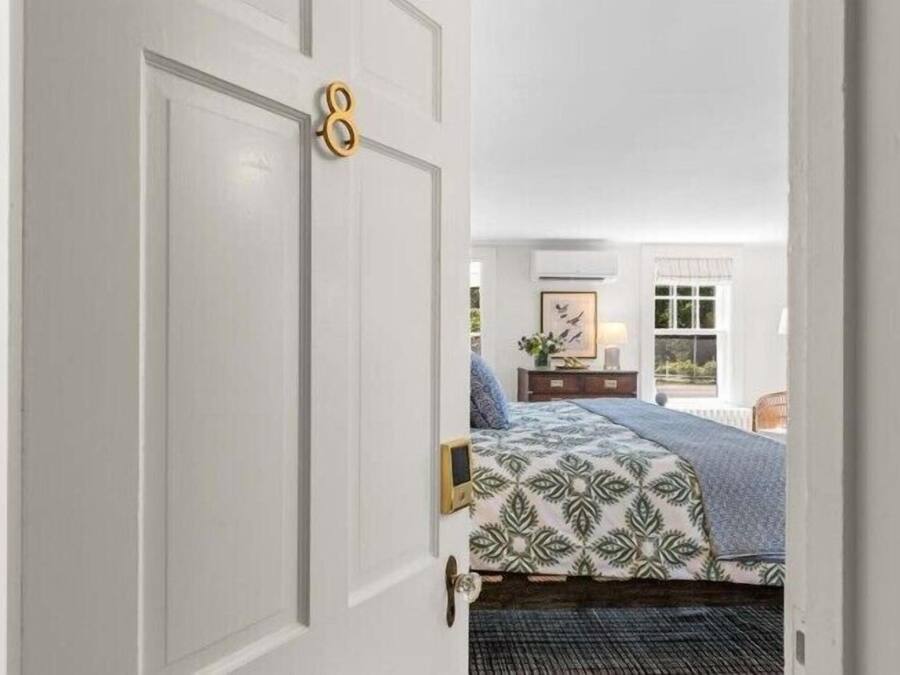 A bedroom with a bed, a dresser, a window, and a door with a number.