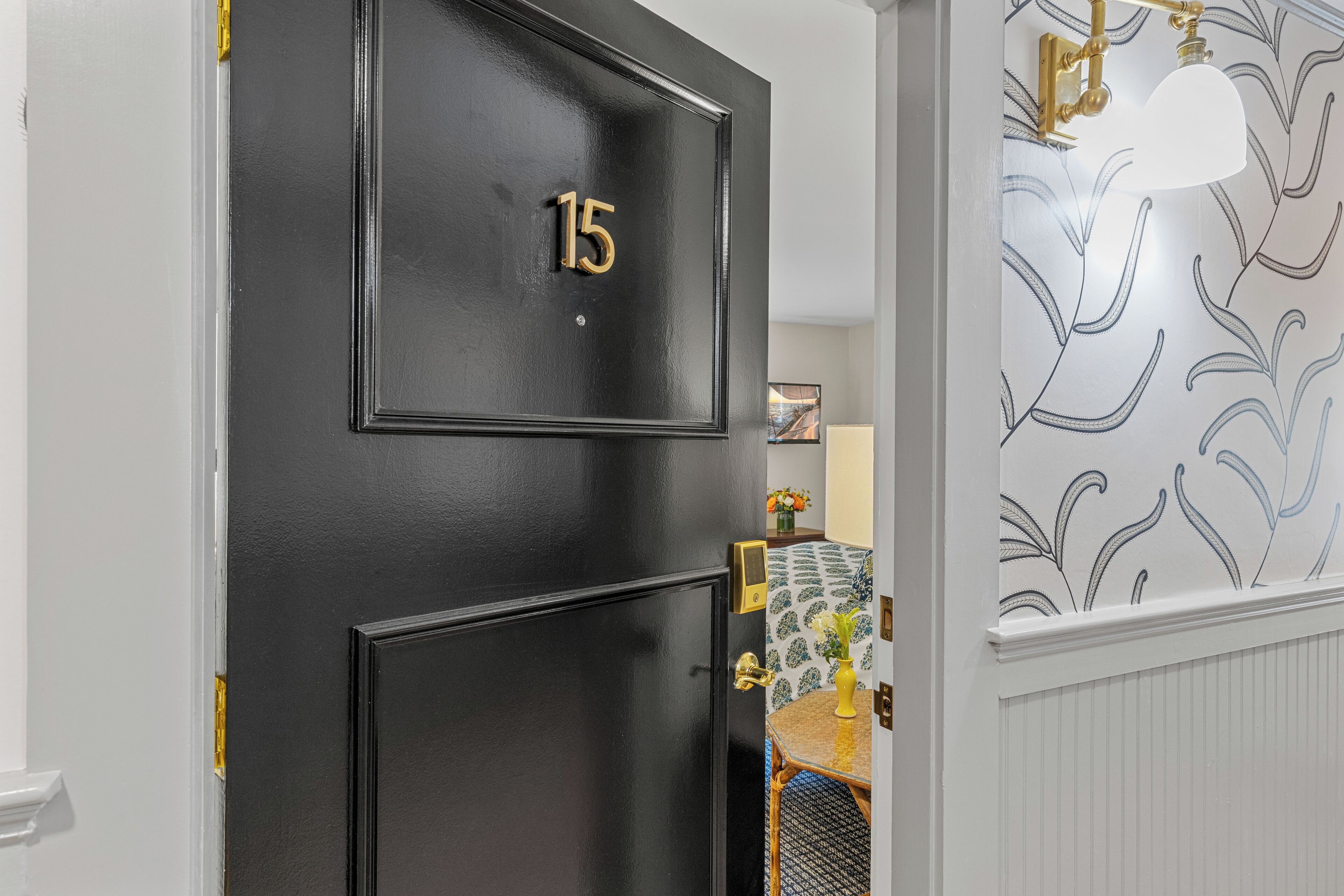Una porta nera con il numero 15, una campanella in ottone e uno sfondo decorato con motivi a foglia.