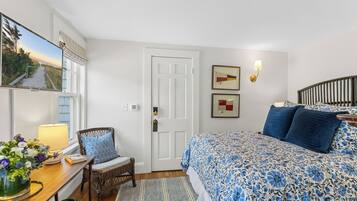 A bedroom with a bed, a chair, a desk, a lamp, a vase with flowers, and a door.