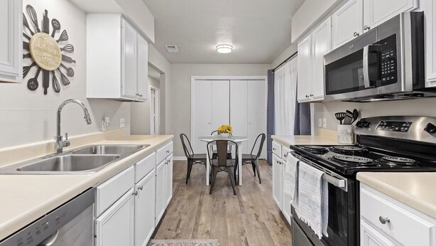 A modern kitchen with white cabinets, stainless steel appliances, and a wooden floor.