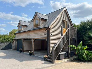 A two-story wooden house with a sloped roof, a front porch, and a staircase leading to the upper level.