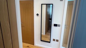 A hallway with wooden flooring, a wooden door, and a mirror on the wall. - Charming Countryside Barn Retreat – Perfect for Relaxing Escapes (East Preston)