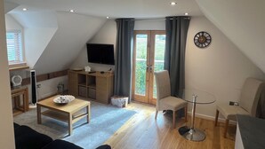 A cozy, well-lit room with a wooden table, a TV, and a comfortable chair. - Charming Countryside Barn Retreat – Perfect for Relaxing Escapes (East Preston)