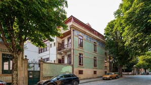 A multi-story building with a green and beige facade, a balcony on the second floor, and a cobblestone street in front. - Central Porto Hideaway with Sunny Terrace by Lisbeyond (Porto)