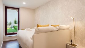 A bedroom with a bed, pillows, a nightstand, a lamp, and a view of a balcony with plants. - Central Porto Hideaway with Sunny Terrace by Lisbeyond (Porto)