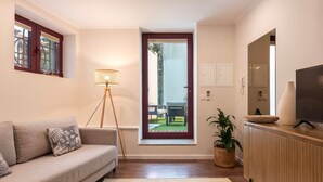 A living room with a sofa, a floor lamp, a television, and a view of an outdoor patio. - Central Porto Hideaway with Sunny Terrace by Lisbeyond (Porto)
