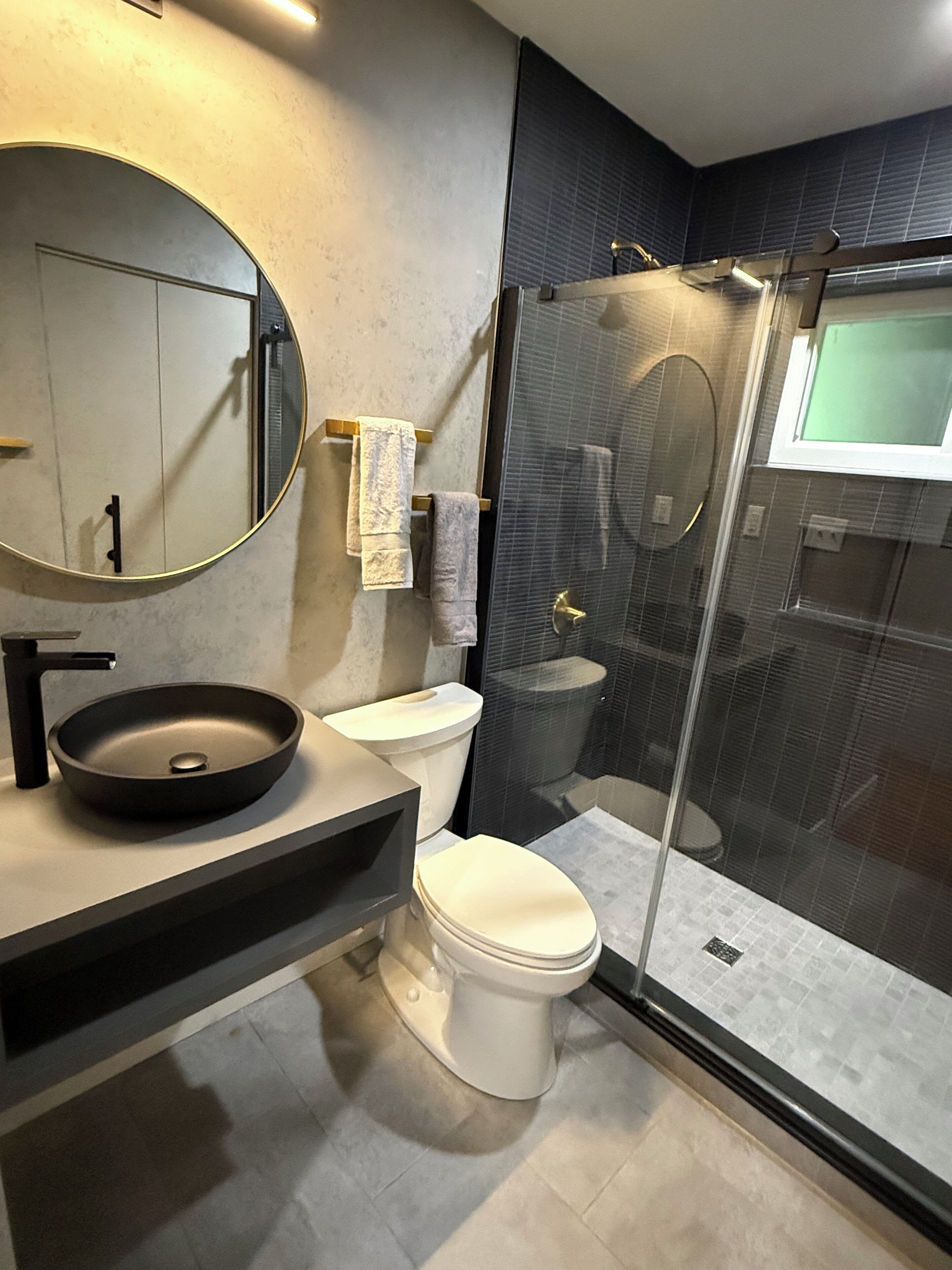A modern bathroom with a round sink, a toilet, and a glass-enclosed shower.