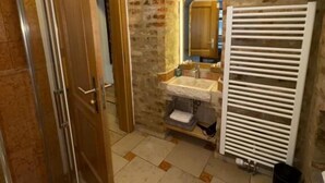 Un baño con pared de piedra, puerta de madera, suelo de baldosas y radiador blanco.