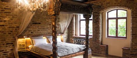 A four-poster bed with a canopy, a chandelier, and a large arched window with a view of greenery.