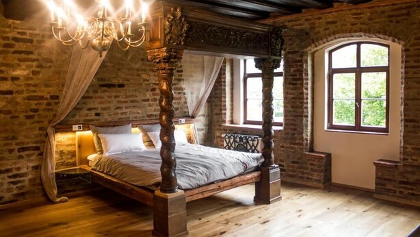 Una cama con dosel, un candelabro y un ventanal con vistas a la vegetación.