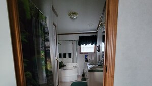 Un pasillo estrecho que conduce a un baño con ducha, lavamanos y ventana.