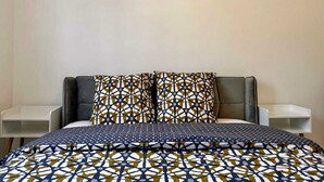 Ein Schlafzimmer mit einem Bett, zwei gleichartige Kissen mit Muster, einer gesteppten Bettdecke mit geometrischem Muster und einem an der Wand hängenden Gemälde eines Löwen.