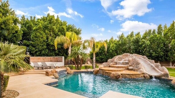 A swimming pool with a waterfall feature, surrounded by palm trees and a lounge area with sun loungers. - Amazing Litchfield Estate With Backyard Oasis! (Litchfield Park)