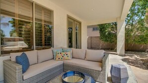 A covered outdoor seating area with a wicker sofa, a round table, and a small side table. - Amazing Litchfield Estate With Backyard Oasis! (Litchfield Park)