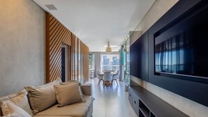 A modern living room with a large flat-screen TV, a sofa, and a dining area in the background. - Sophisticated Stay 200m From Praia Brava - EHI (Itajai)