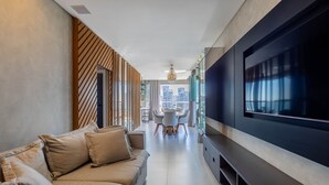 Una sala de estar moderna con un televisor de pantalla plana grande, un sofá y un comedor al fondo.