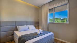 Ein modernes Hotelzimmer mit einem großen Bett, Blick auf einen Turm und einem Fenster mit Jalousien.